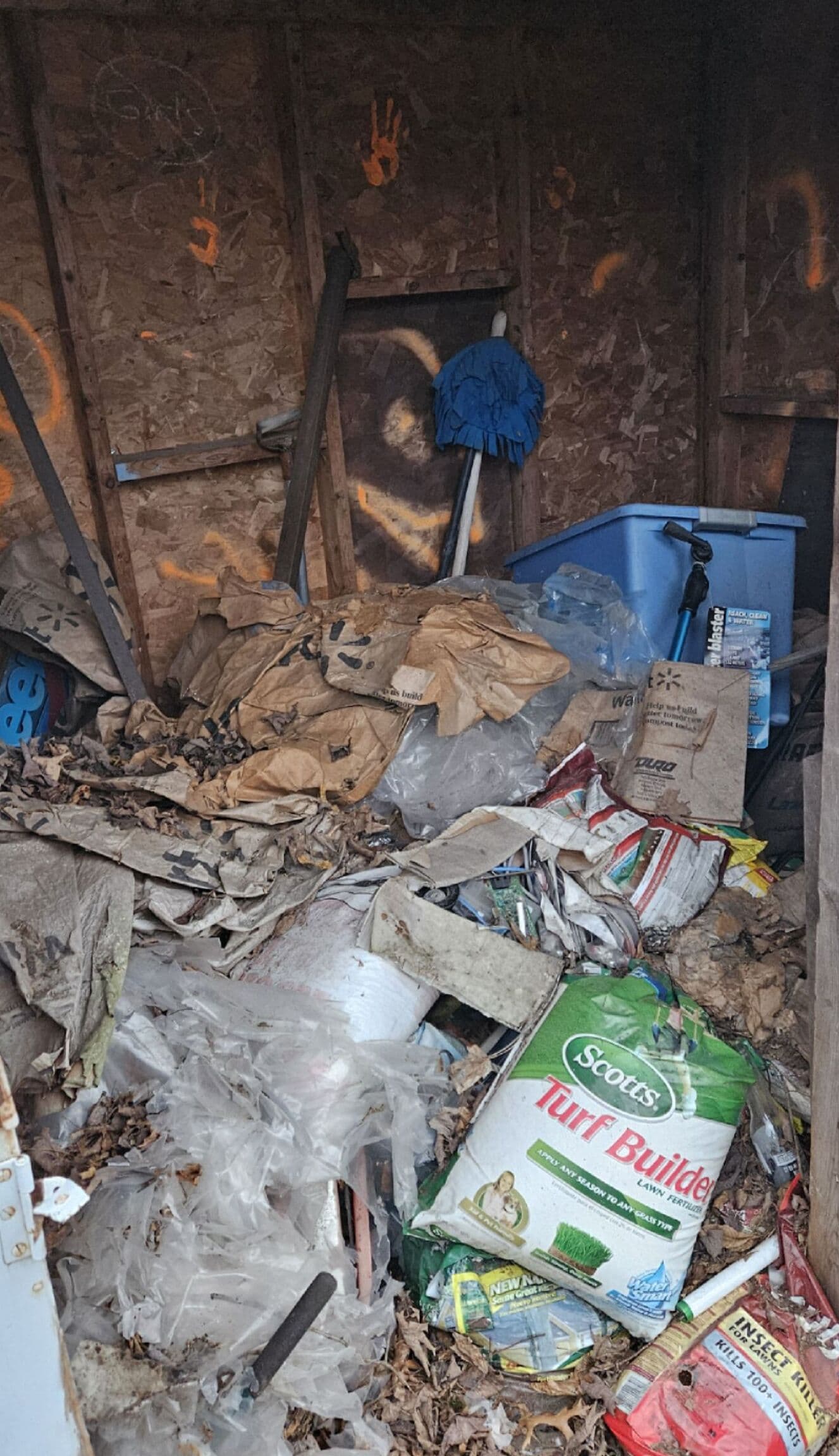 Cluttered shed interior filled with trash, tools, and scattered gardening supplies.