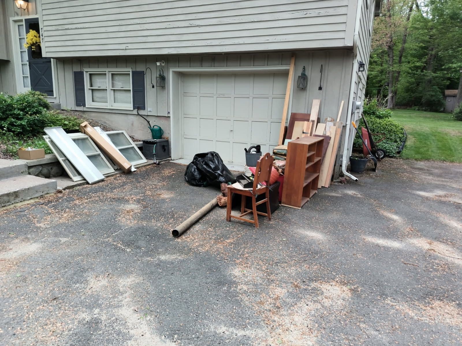Piles of discarded furniture and debris outside a garage on a gravel driveway.