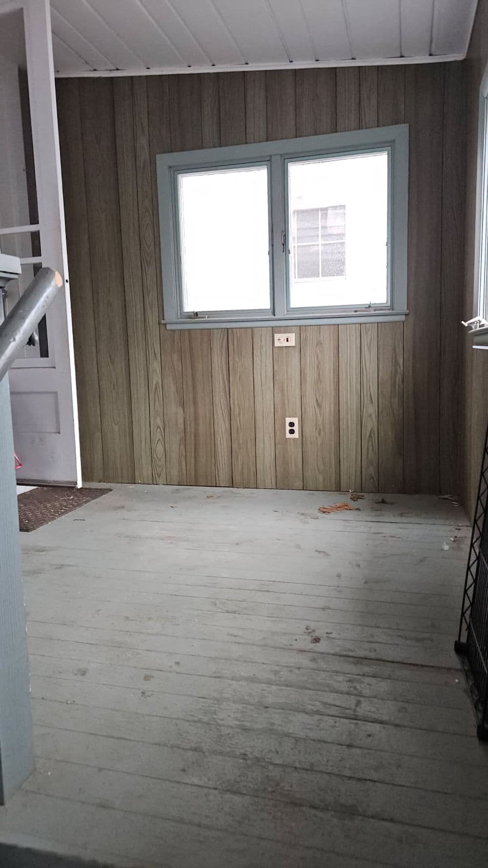 Empty room with wooden paneling, two windows, and light gray flooring. Ideal for renovations.