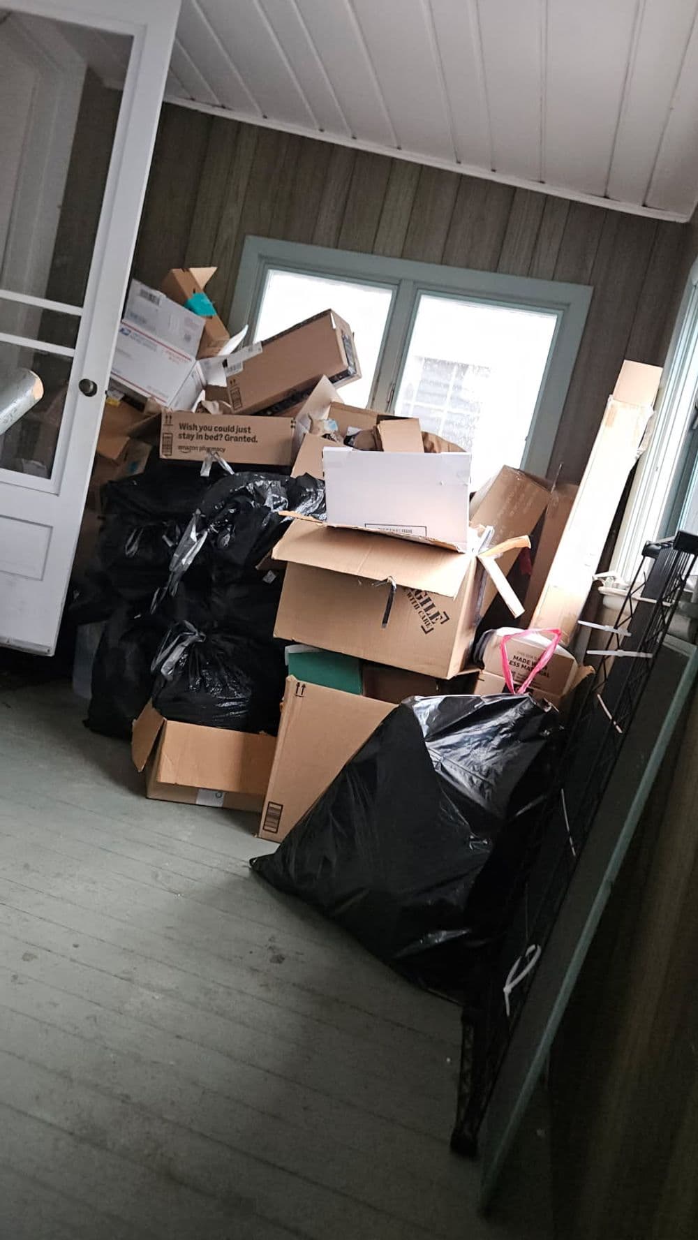 Cluttered room filled with stacked cardboard boxes and black garbage bags.