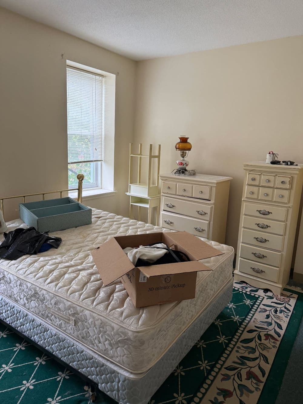 Unmade bedroom with a mattress, unpacked boxes, and vintage furniture in natural light.